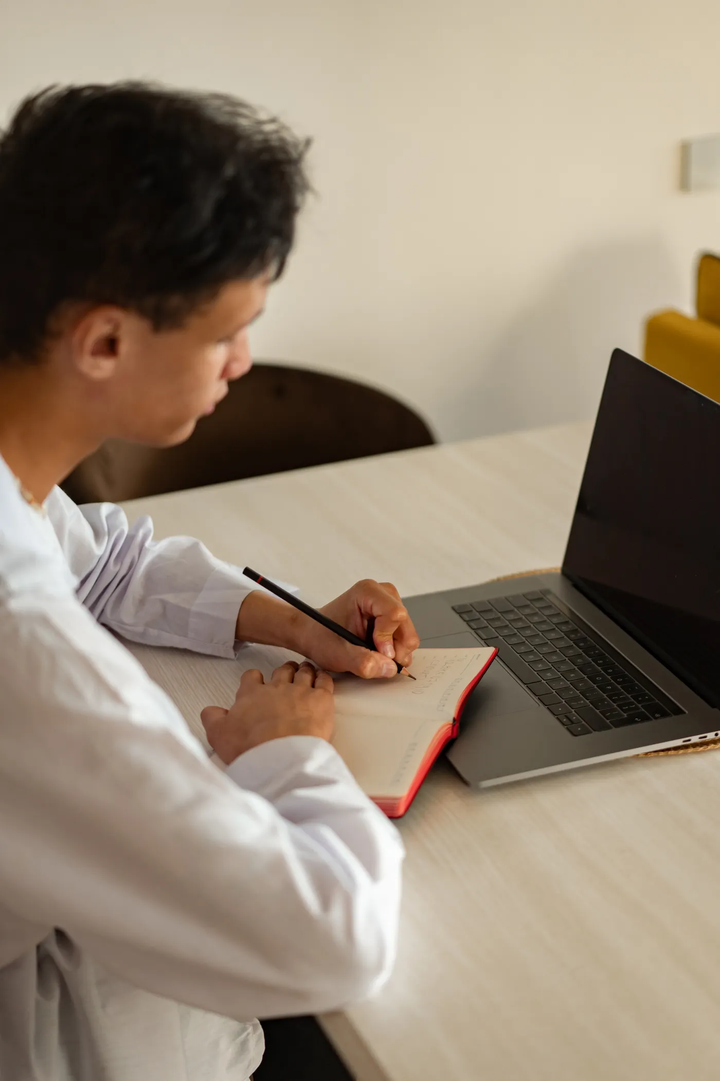 Adult student studying at a laptop with a notebook in a home workspace